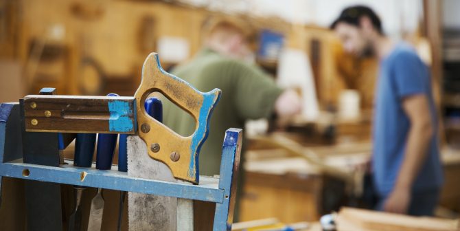 Close up of hand tools in boat-builder’s workshop, two men working in background. Close up of hand tools in boat-builder's workshop, two men working in background.